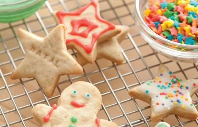 Fotografia de biscoitos decorados de natal em formato de boneco, estrela e presentes, nas cores vermelho, verde e branco, decorados com confeitos das mesmas cores.