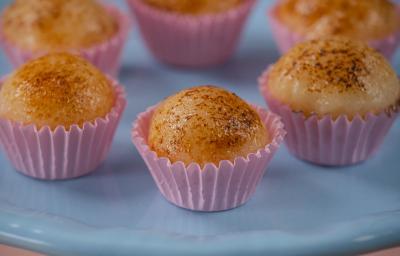 Fotografia de seis unidades de embalagens rosas, uma perto da outra, formando um hexágono. em cada forminha, tem um brigadeiro de creme brulée. As embalagens estão sobre um apoio de cor azul claro.