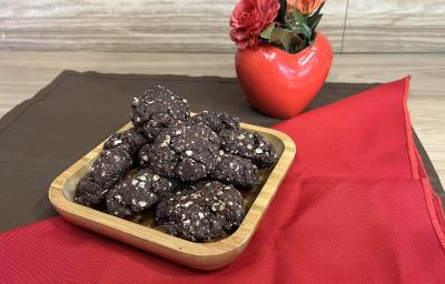 Fotografia em tons de vermelho e marrom com um recipiente de madeira ao centro. Dentro do recipiente existe vários cookies de NESCAU com NESTLÉ Aveia Flocos!