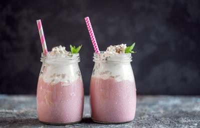 Fotografia de dois recipientes decorativos de vidro com frapê com Leite MOÇA, guaraná e suco de limão. No mesmo copo tem um canudo rosa e branco e hortelã.