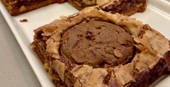 Fotografia mostra um brownie de chocolate com um cookie de chocolate em cima.