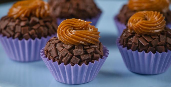 Fotografia de cinco unidades de forminhas azuis com brigadeiro de pão de mel, com doce de leite por cima de cada unidade. Os brigadeiros estão sobre um apoio decorativo de cor azul.