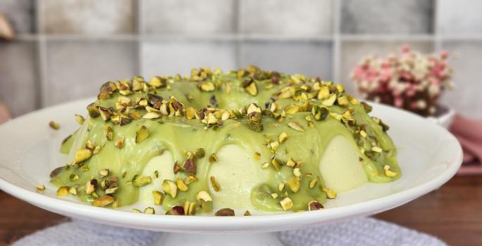 Fotografia de um pudim de pistache em tons verdes sobre um prato branco.