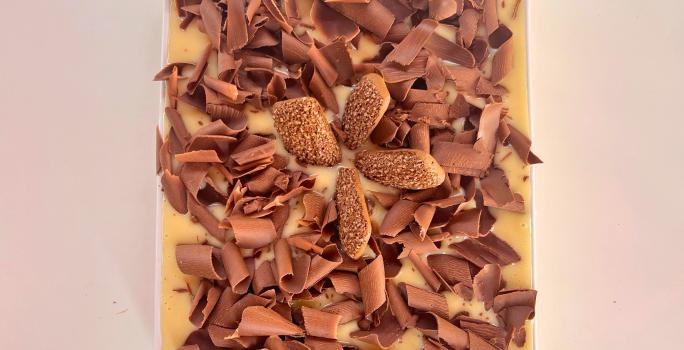 Fotografia mostra um pavê com raspas de chocolate branco e biscoito champanhe de chocolate ao centro.