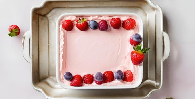 Fotografia vista de cima de um recipiente branco quadrado com uma paleta mexicana de travessa, com morangos por cima, dentro de uma forma de alumínio.