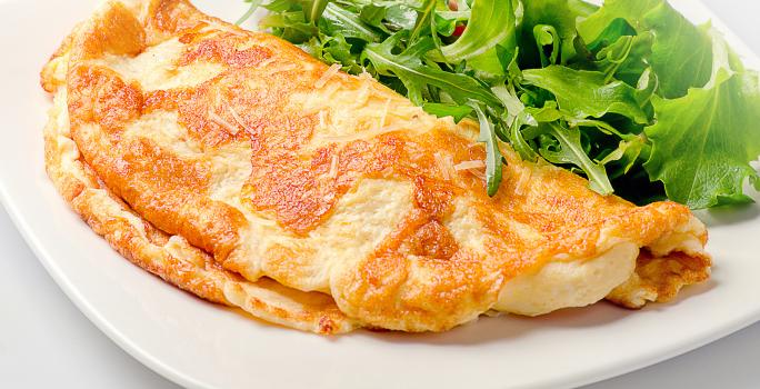 Foto aproximada de uma omelete dobrada ao meio e servida com algumas folhas verdes em um prato. Esta omelete foi prepara na airfryer de acordo com a receita.