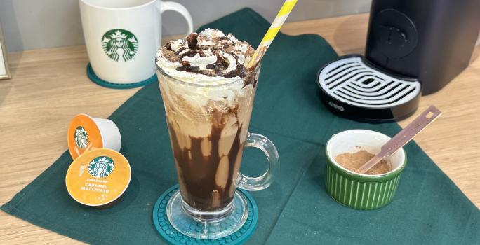 Foto da receita de Frapê de Chocolate. Obseva-se um copo grande decorado com calda de chocolate e chantilly e, ao lado esquerdo, cápsulas de Starbucks.