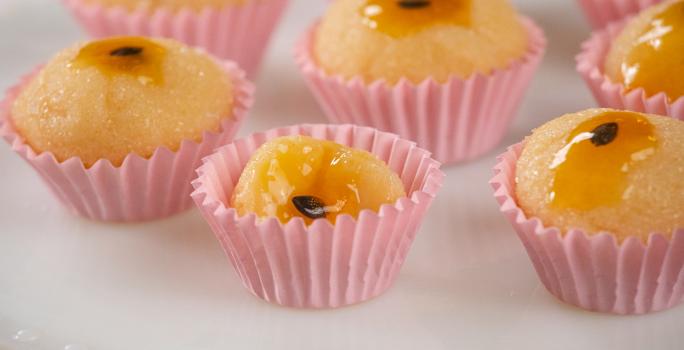 Fotografia em tons de rosa com várias forminhas de brigadeiro ao centro. Dentro de cada forminha existe brigadeiros feitos de maracujá finalizados com geleia de maracujá no topo.