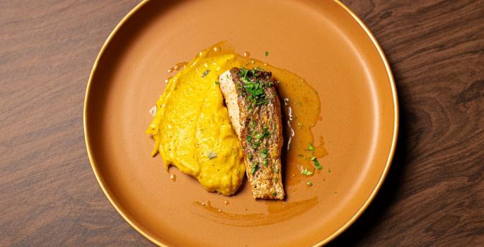 Foto da Receita de Robalo com Azeite de Ervas e Purê de Abóbora do Masterchef 11. Observa-se uma foto de cima do prato com o purê bem amarelo à esquerda, servido com o peixe finalizado com salsinha.