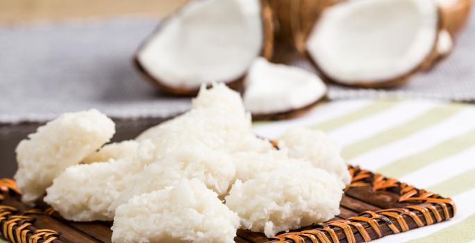 Foto da receita de Cocada Zero Lactose. Observa-se as cocadas dispostas em uma tábua e atrás é possível ver os cocos abertos.