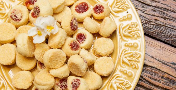 Fotografia de um prato amarelo de vidro sobre uma mesa de madeira. Dentro do prato tem várias unidades de biscoitos amanteigados com goiabada.