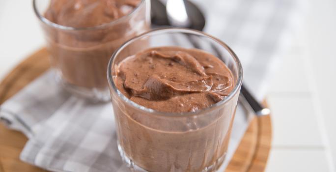 Receita de Mousse de Chocolate da Tia Alzira, tradicional e prático, feito com Chocolate Meio Amargo NESTLÉ CLASSIC, NESTLÉ Creme de Leite e claras em neve, servido em copinhos sobre uma mesa com uma tábua de madeira e colheres ao fundo