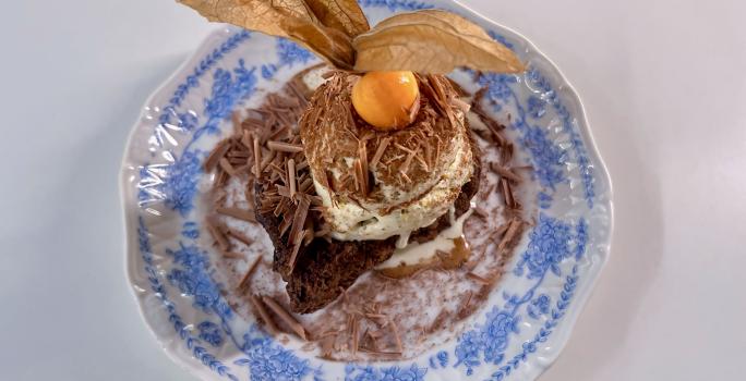 Fotografia em tons de branco com um prato azul ao centro. Em cima do prato existe uma receita de rabanada de panettone com uma bola de sorvete de creme em cima