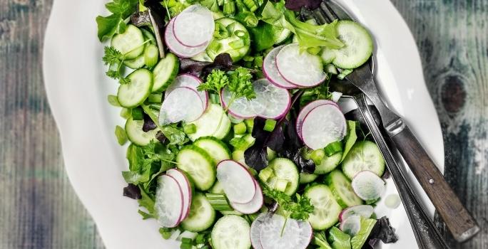 Fotografia vista de cima de um recipiente de vidro raso branco, com uma salada de acelga com cebolinha-verde com tempero, vinagre, azeite e limão.