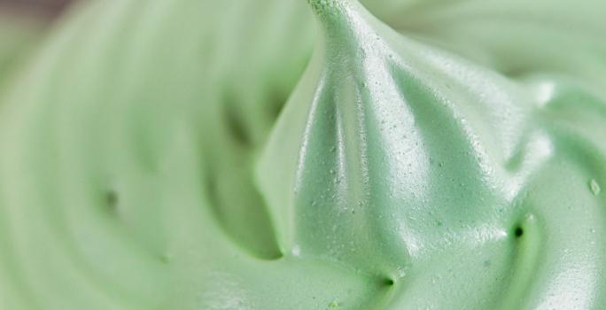 Fotografia de uma cobertura de consistência mais densa, de cor esverdeada, feita com leite MOÇA e erva cidreira.