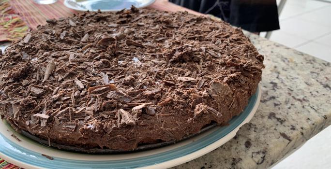 Fotografia de uma torta de chocolate com raspas de chocolate sobre um apoio branco com borda azul.