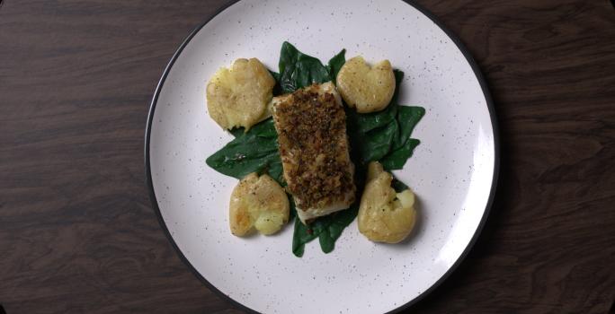 Fotografia em tons de branco com um prato branco ao centro. Dentro do prato existe uma receita de bacalhau acompanhado de batatas amassadas e espinafre.