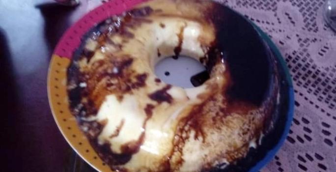 Fotografia de um bolo de sorvete com calda de açúcar e chocolate sobre um apoio colorido e uma mesa escura.