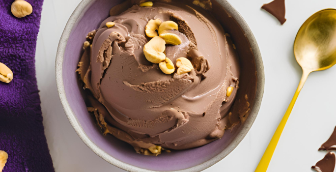 Fotografia em tons de branco com uma tigela ao centro. Dentro da tigela existe um sorvete de chocolate com pedaços de amendoim em cima.