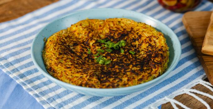 Fotografia em tons de azul com um prato azul ao centro. Em cima do prato existe uma receita de batata-doce rosti recheada com carne desfiada