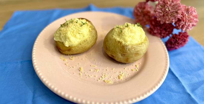 Fotografia em tons de azul e rosa com um prato rosa ao centro. Dentro do prato existe duas batatas recheadas com creme de ASCENDA e polvilhadas com queijo parmesão