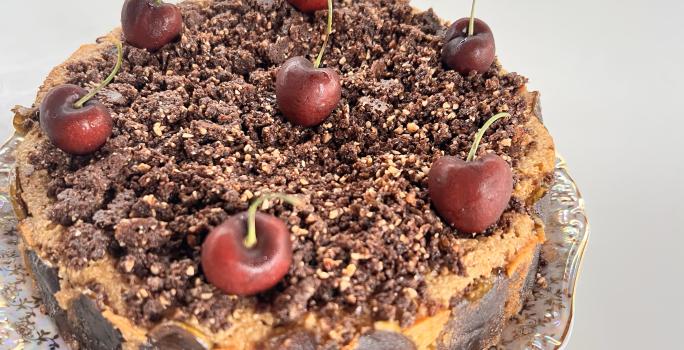 Fotografia em tons de branco com um bolo de Cuca de maçã verde ao centro enfeitada com cerejas