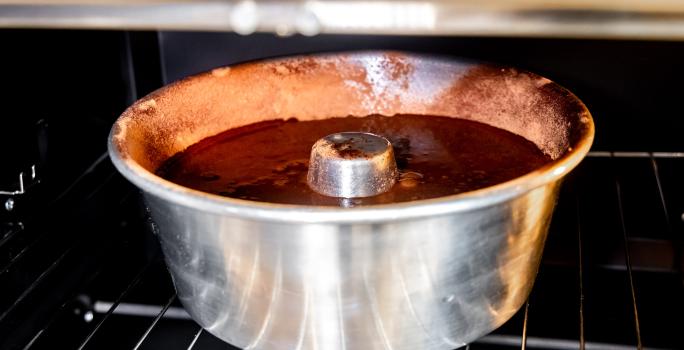 Foto aproximada de uma forma de alumínio de furo central com a massa do bolo dentro. Ela está dentro de um forno.