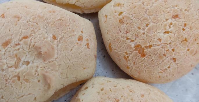 Fotografia de quatro pães de queijo sobre uma forma de alumínio.