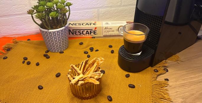 Fotografia em tons de laranja com uma cafeteira ao centro. Ao lado da cafeteira existe um pote com casca de laranjas cristalizadas.