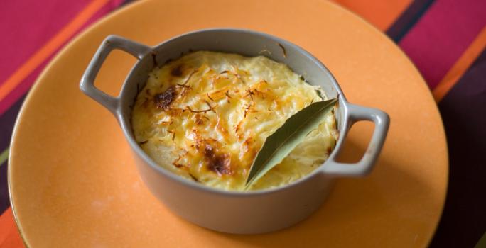 Fotografia de um recipiente pequeno que foi ao forno com uma receita de chuchu recheado com creme de milho e frango. A receita foi gratinada e tem uma folha de louro por cima.