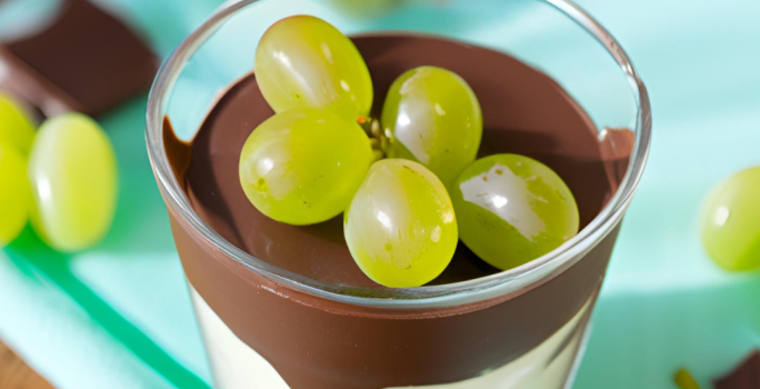 Foto da Receita de Bombom de Uva no Copo. Observa-se um copo de vidro com um creme baixo embaixo, por cima chocolate e decorado com uvas verdes. Foto gerada por IA.