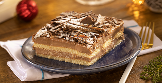 Fotografia mostra um um pavê de chocolate servido em um prato de sobremesa, com suas camadas de chocolate cremoso e biscoito perfeitamente visíveis.