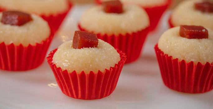 Fotografia de sete unidades de forminhas vermelhas com brigadeiro de romeu e julieta. Por cima de cada um tem um quadradinho de goiabada, e todos estão sobre um apoio decorativo de cor branca.