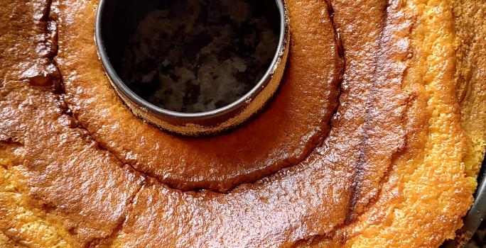 Fotografia de uma forma de bolo preta com furo central com um bolo de cenoura brilhante sobre uma bancada.