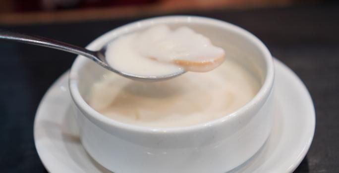 Fotografia de fatias de laranja cobertos por leite condensado dentro de um recipiente branco pequeno, sobre um prato branco pequeno.