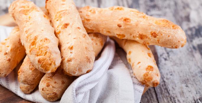 Fotografia em tons de cinza com uma toalha branca ao centro. Em cima da toalha existe vários biscoitinhos de polvilho dourados.