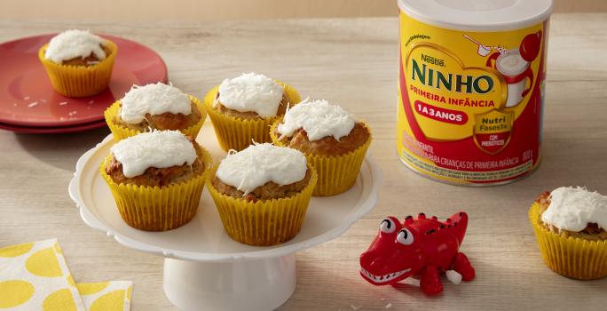 Fotografia em tons de amarelo e vermelho com 5 bolinhos ao centro. Por cima de cada bolinho existe um creme de leite de coco, coco ralado e NINHO Primeira Infância