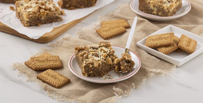 Foto da receita de Blondie de Tostines. Observa-se um prato de sobremesa com uma fatia de blondie com uma colher retirando uma fatia. Biscoitos TOSTINES decoram a foto.