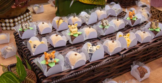 Fotografia de várias forminhas brancas com brigadeiro branco preparado com Leite MOÇA e gema, modelado em formato de animais. As forminhas estão sobre um apoio de madeira trançado.