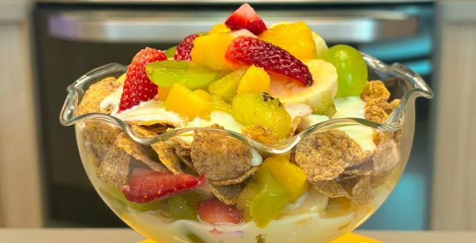 Fotografia em tons de amarelo com uma taça de vidro ao centro. Dentro da taça existe uma receita de salada de frutas com creme de Leite NINHO Adulto e Nesfit Cereal