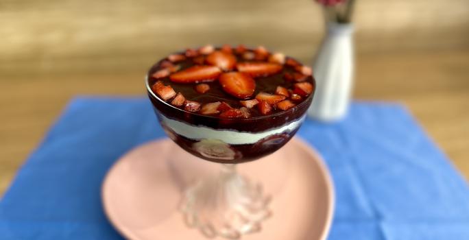 Fotografia em tons de rosa e azul com uma taça de vidro ao centro. Em cima da taça existe uma receita de açaí com frutas e ASCENDA