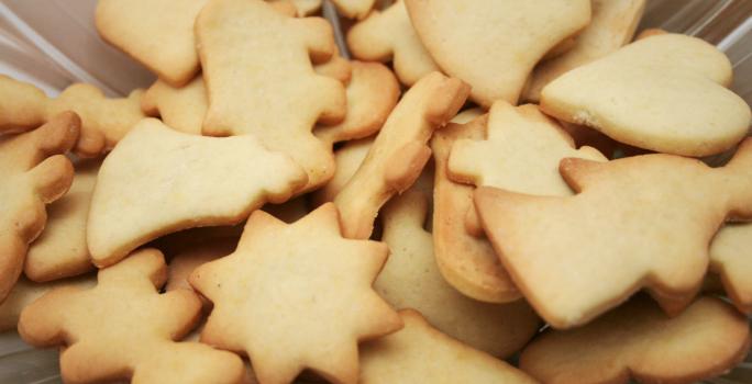 Fotografia em tons de caramelo com vários biscoitos amanteigados ao centro. Cada biscoitinho tem um formato diferente.