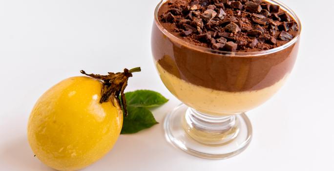 Receita de Mousse de Maracujá com Chocolate, fácil e delicioso, feito com Leite MOÇA, suco e maracujá concentrado, NESTLÉ Creme de Leite e Chocolate ao Leite NESTLÉ CLASSIC, servido em uma taça ao lado de uma maracujá