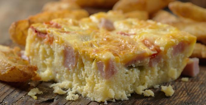 Fotografia de uma torta de panqueca recheada cortada em pedaços, sobre uma tábua de madeira.