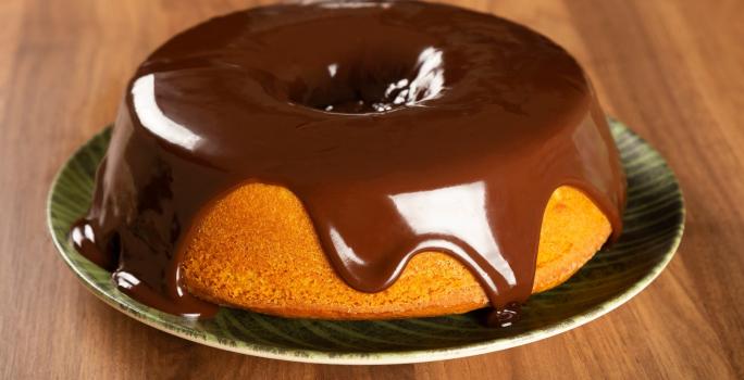 Foto da receita de Bolo de Cenoura. Observa-se o bolo em um prato de porcelana com calda de chocolate por cima escorregando.