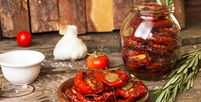 Fotografia em tons de marrom com um pote de vidro ao centro. Dentro do pote existe uma receita de tomate seco feita na Air Fryer