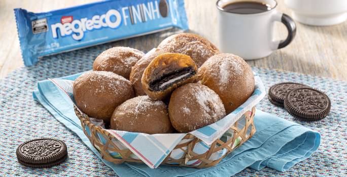 Fotografia mostra uma cestinha com bolinhos de chuva recheado com biscoito. No fundo um pacote de biscoito e uma xícara de café.