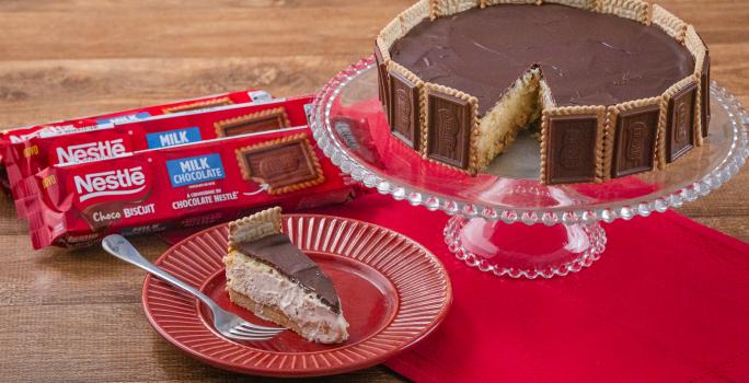 Fotografia em tons de vermelho com uma torta holandesa ao centro feita com Biscoito Choco Biscuit. Ao fundo existe três pacotes de biscoito Choco Biscuit NESTLÉ