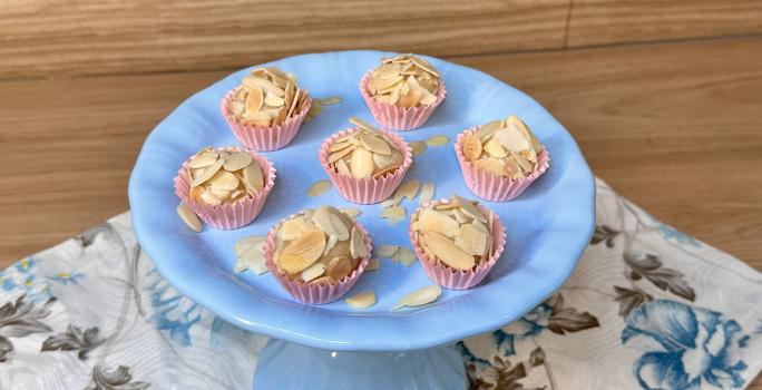 Fotografia em tons de azul e rosa com um prato azul ao centro. Em cima do prato, existe 7 brigadeiros de caramelo salgado cobertos com amêndoas laminadas.