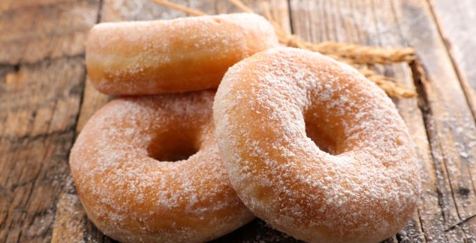 Fotografia de três rosquinhas, uma apoiada na outra, passadas no açúcar de confeiteiro, sobre uma mesa de madeira.